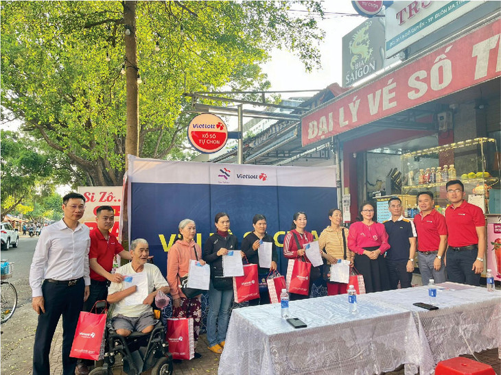 Đại diện Vietlott và đại diện Quỹ Tâm Tài Việt trao thẻ bảo hiểm cho điểm bán hàng xổ số tự chọn và người phân phối vé số