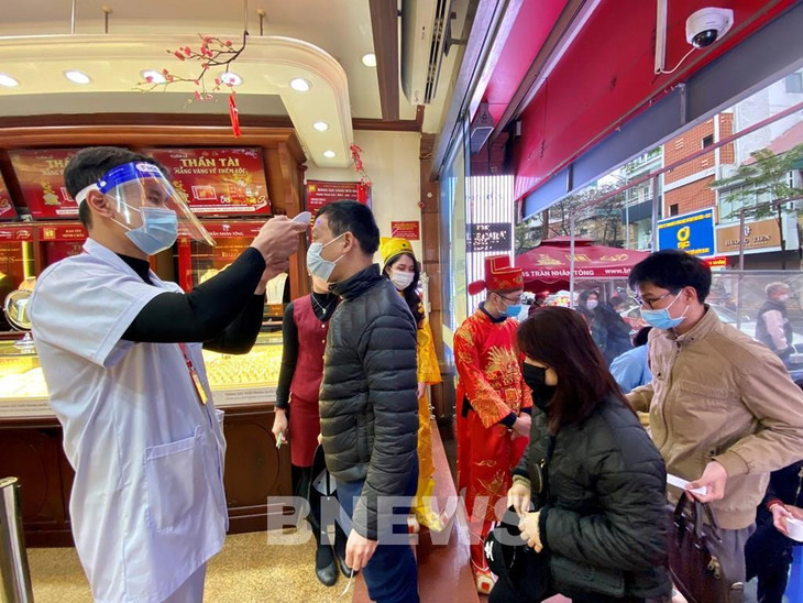 Khách hàng thực hiện đo thân nhiệt trước khi vào giao dịch mua sắm tại các điểm bán vàng. Ảnh: Diệp Anh/BNEWS/TTXVN
