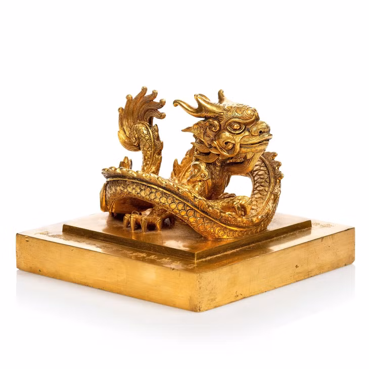 Quai ấn vàng của vua Minh Mạng đúc hình một con rồng uốn khúc, đầu ngẩng cao, mắt nhìn về phía trước, tư thế vững vàng Quai ấn vàng của vua Minh Mạng đúc hình một con rồng uốn khúc, đầu ngẩng cao, mắt nhìn về phía trước, tư thế vững vàng