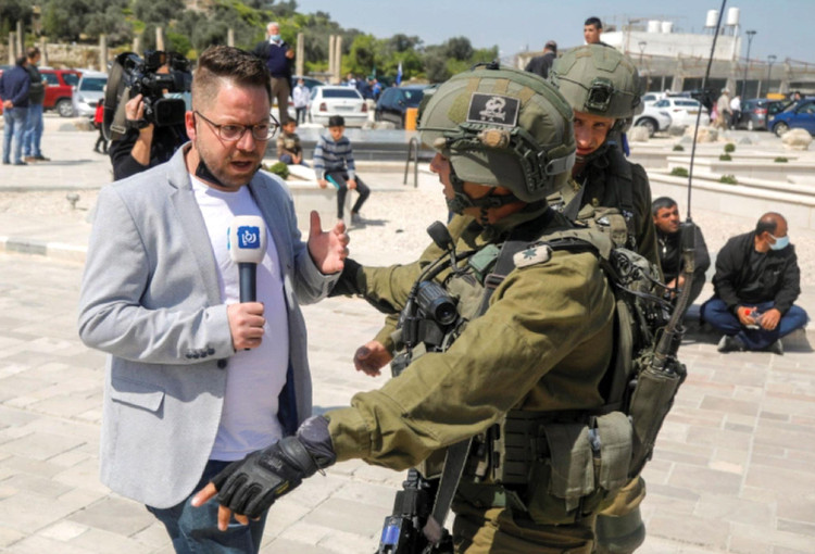 Một phóng viên truyền hình đối diện quân lính Israel tại khu vực Bờ Tây vào tháng 3/2021
