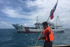 Một nhà hoạt động Philippines giơ cao lá cờ của nước này khi một tàu bảo vệ bờ biển Trung Quốc đi qua. Ảnh:AFP