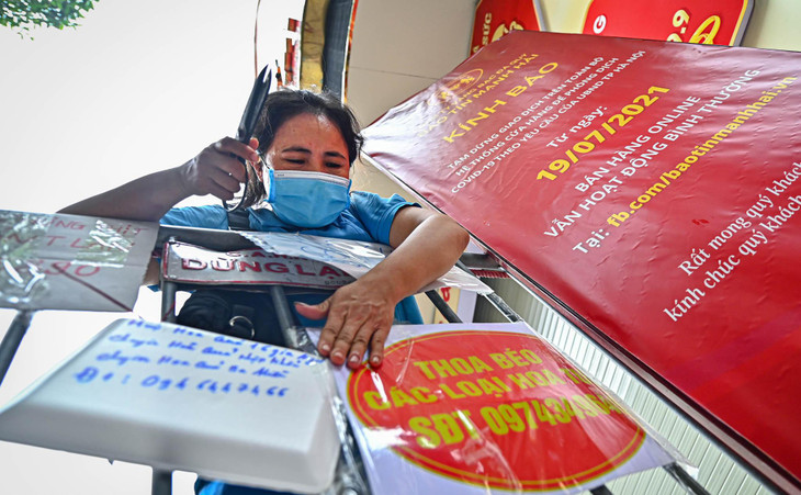 Một tiểu thương đang hoàn thiện việc dán tấm biển quảng cáo trên hàng rào chắn để người dân có thể liên hệ mua các mặt hàng thiết yếu.