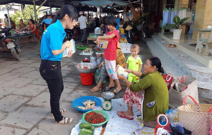 Cán bộ BHXH huyện Trà Cú phát tờ rơi và tuyên truyền cho người dân các nhóm chợ