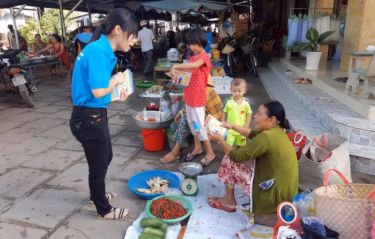 Cán bộ BHXH huyện Trà Cú phát tờ rơi và tuyên truyền cho người dân các nhóm chợ