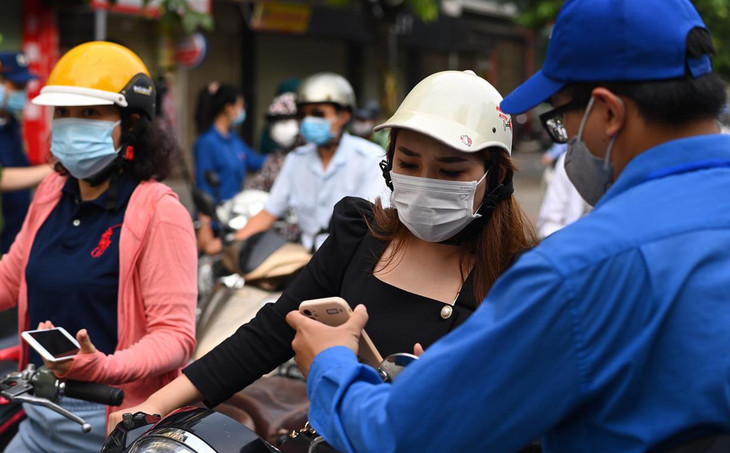 Theo quy định, người ra đường, đến công sở làm việc khi đi qua chốt kiểm soát phải xuất trình giấy tờ cho phép đi lại có đóng dấu của cơ quan chủ quản. Trong ảnh một phụ nữ cho bảo vệ xem giấy tờ chứng nhận được chụp lại qua điện thoại.