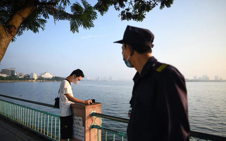 Một người nán lại chụp ảnh buổi sáng ven hồ Tây được lực lượng chức năng nhắc nhở đi về.