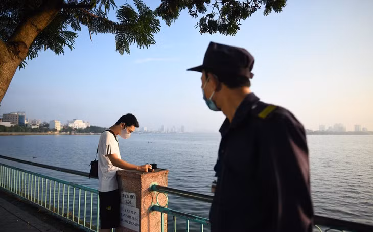 Một người nán lại chụp ảnh buổi sáng ven hồ Tây được lực lượng chức năng nhắc nhở đi về.