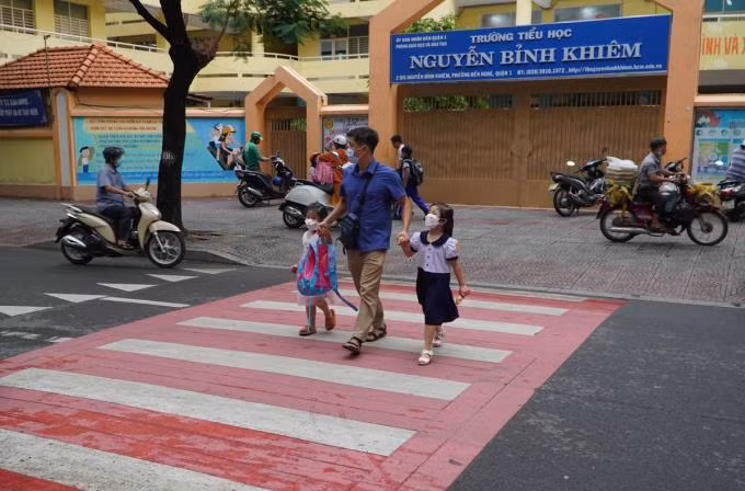 Phụ huynh dắt con qua đường Nguyễn Bỉnh Khiêm, trước trường tiểu học mới sơn phản quang màu đỏ