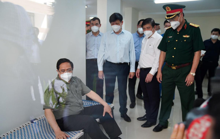 Thủ tướng Phạm Minh Chính ngồi thử trên chiếc giường gấp dành cho bệnh nhân lẫn lực lượng y tế ở bệnh viện dã chiến.