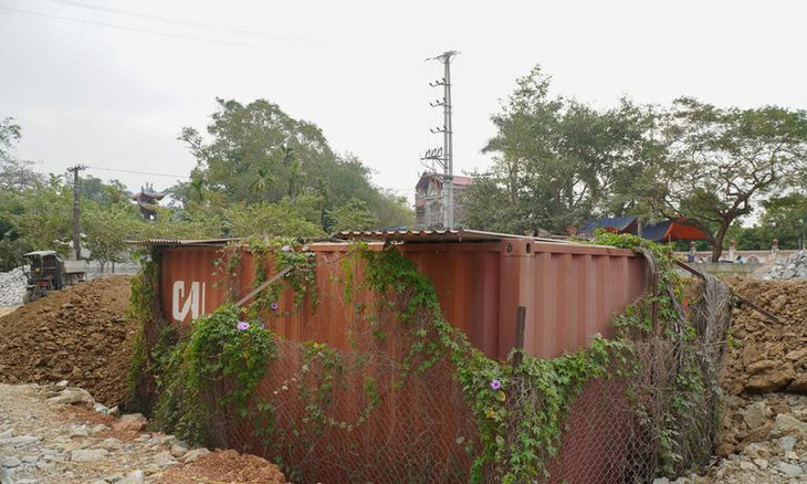 Sau một thời gian dài nằm phơi mưa phơi nắng, thùng container đựng lô gỗ sưa &quot;trăm tỷ&quot; hoa cỏ quấn xung quanh, giờ nằm lọt thỏm dưới nền đất nhà văn hóa thôn Phụ Chính