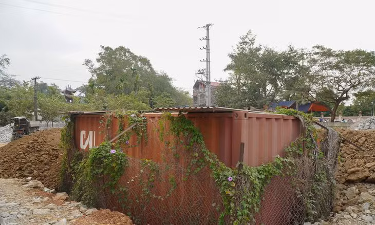Sau một thời gian dài nằm phơi mưa phơi nắng, thùng container đựng lô gỗ sưa "trăm tỷ" hoa cỏ quấn xung quanh, giờ nằm lọt thỏm dưới nền đất nhà văn hóa thôn Phụ Chính