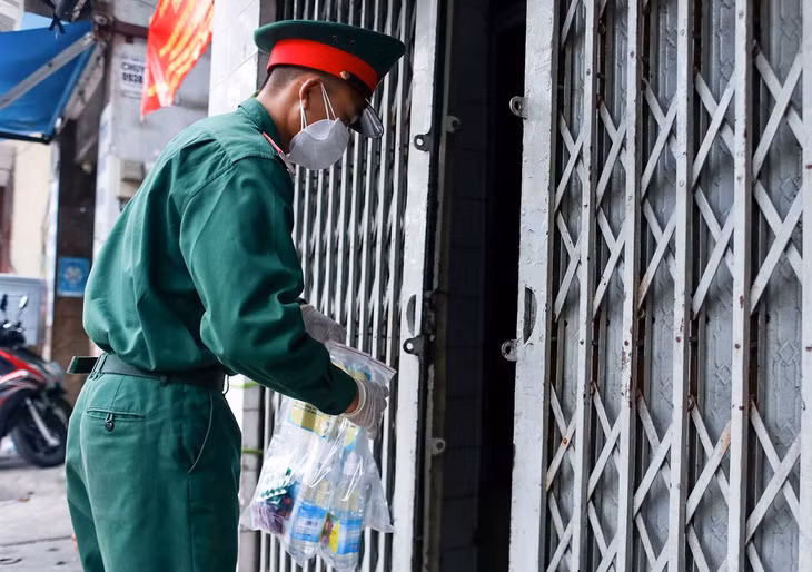 Một chiến sĩ trao thuốc cho một gia đình có 6 ca F0 đang tự điều trị tại nhà trên đường An Dương Vương (Quận 5)