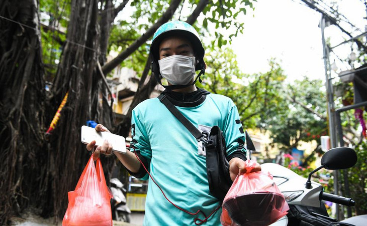 Anh Tiến Đặng (shipper) vừa lấy xong đơn hàng, chuẩn bị giao cho khách. “Buổi trưa là giờ cao điểm nhất đối với các tài xế chúng tôi. Có những cửa hàng nhiều đơn, phải chờ tới 30 phút mới đến lượt. Nhiều người sốt ruột đã xảy ra tình trạng chen lấn”, anh chia sẻ. Khi gặp phải những trường hợp quá đông người, anh Tiến Đặng lựa chọn nhắn tin báo với khách rồi xếp hàng để chờ tới lượt.