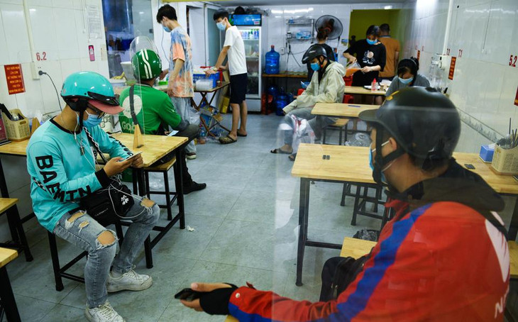 Bên trong một tiệm cơm gà trên phố Chùa Láng, các shipper được hướng dẫn ngồi chờ đơn tại các bàn ăn lắp tấm chắn giọt bắn. Chủ cửa hàng chia sẻ: “Tôi mời họ ngồi tại bàn có vách ngăn vừa là cách phòng dịch tốt mà họ cũng đỡ vất vả phải đứng chờ”.