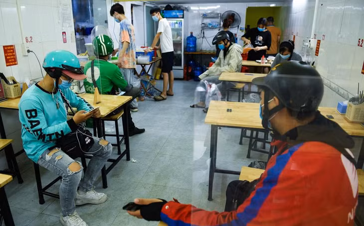 Bên trong một tiệm cơm gà trên phố Chùa Láng, các shipper được hướng dẫn ngồi chờ đơn tại các bàn ăn lắp tấm chắn giọt bắn. Chủ cửa hàng chia sẻ: “Tôi mời họ ngồi tại bàn có vách ngăn vừa là cách phòng dịch tốt mà họ cũng đỡ vất vả phải đứng chờ”. Bên trong một tiệm cơm gà trên phố Chùa Láng, các shipper được hướng dẫn ngồi chờ đơn tại các bàn ăn lắp tấm chắn giọt bắn. Chủ cửa hàng chia sẻ: “Tôi mời họ ngồi tại bàn có vách ngăn vừa là cách phòng dịch tốt mà họ cũng đỡ vất vả phải đứng chờ”.